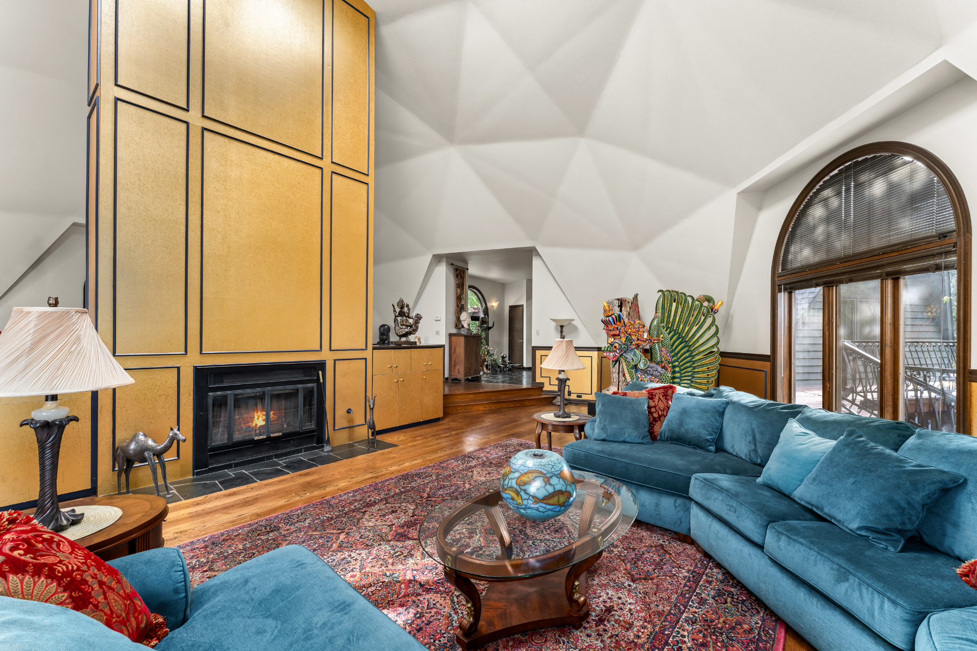 Living room beneath the faceted geodesic ceiling, with gold-paneled hearth, blue sectional, and arched windows