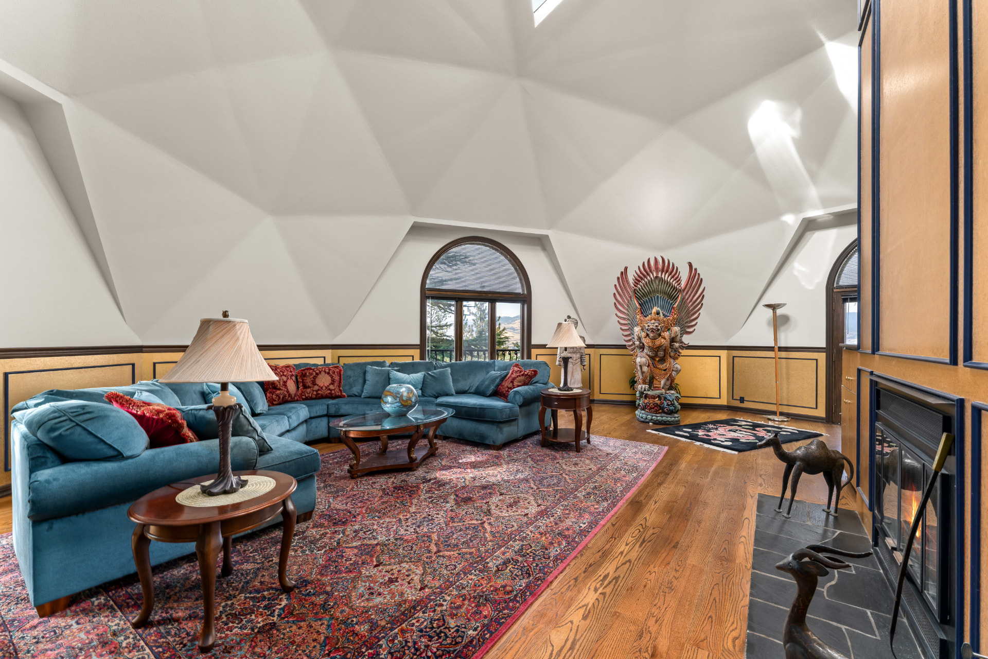 Wide living room beneath the faceted geodesic ceiling with curved blue seating and gold-paneled hearth