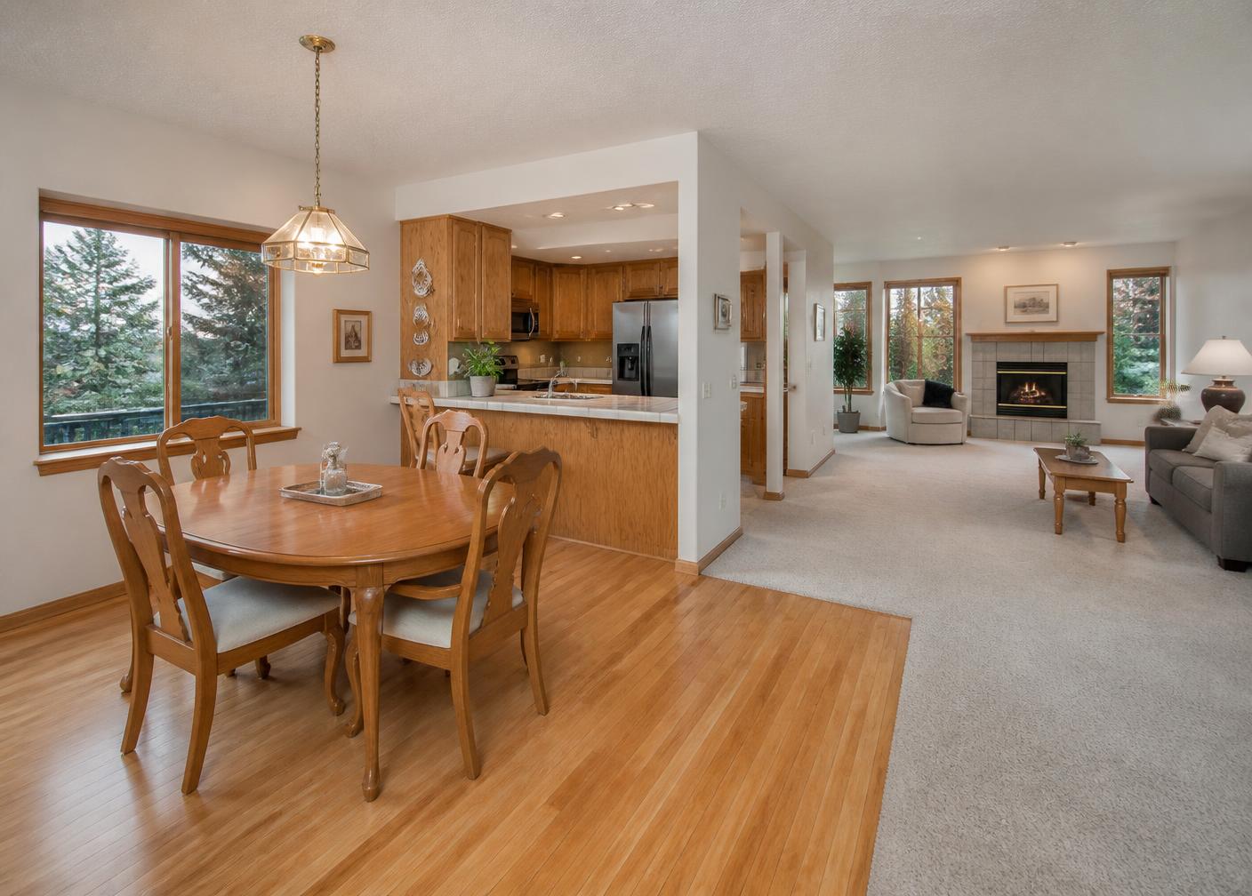 Open living and dining area with oak kitchen cabinets, updated stainless appliances, hardwood and carpet floors, and windows facing evergreens