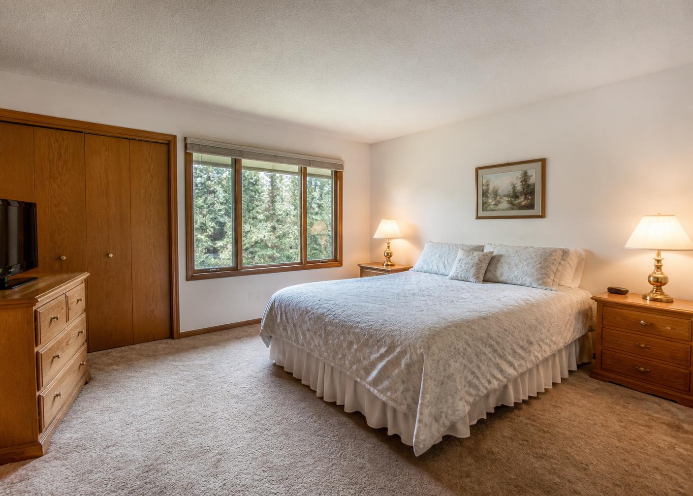 Primary bedroom with painted walls, oak trim and closet doors, carpet, and a window overlooking tall evergreen trees